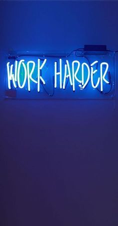 a neon sign that says work harder on the side of a blue wall with writing underneath it