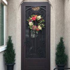 the front door is decorated with flowers and greenery, along with two potted trees