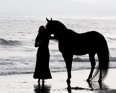 a woman standing next to a horse on top of a sandy beach near the ocean