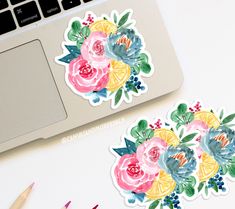 two stickers with watercolor flowers on them next to a computer keyboard and pencils