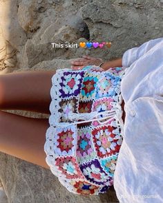 a woman is sitting on the rocks with her hand in her pocket and crocheted shorts