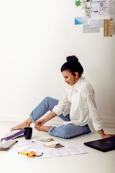 a woman is sitting on the floor with her laptop and papers around her, holding a coffee cup