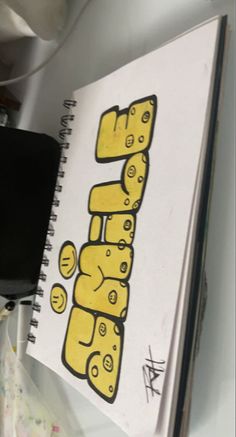 an open notebook with the letter h drawn in yellow and black on top of it