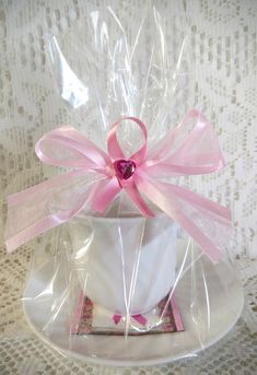 a white cup with a pink bow on it sitting on top of a saucer