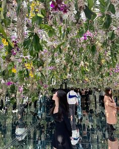 two women are standing in front of a mirrored wall with flowers hanging from the ceiling