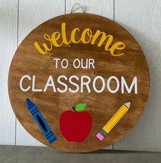 a wooden sign with the words welcome to our classroom and an apple, crayons, and pencils