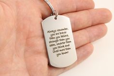 a hand holding a white dog tag that says always remember you are never afraid to believe