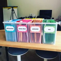 three plastic bins with labels on them are sitting on a table in an office