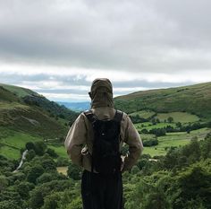 a man standing on top of a lush green hillside next to a lush green valley