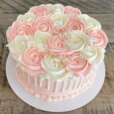 a cake decorated with pink and white frosting roses on top of a wooden table