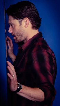 a man is standing in front of a blue wall and talking on his cell phone