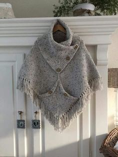 a knitted ponchle hanging on a white door with buttons and fringes