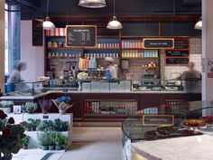 the inside of a restaurant with people working behind the counter and plants on the shelves