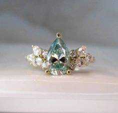 an aqua and white diamond ring sitting on top of a table