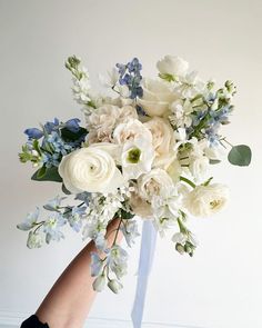 a bouquet of white and blue flowers is being held by someone's hand on the floor