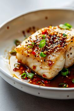 a white plate topped with fish covered in sauce and garnished with green onions