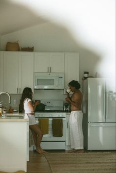 two people standing in a kitchen with white cabinets and an open stove top oven next to each other