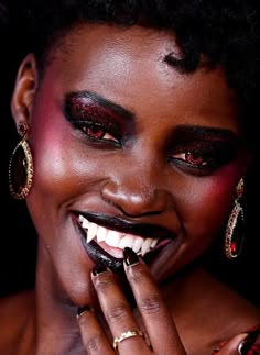 a close up of a person with black makeup and rings on her finger, smiling