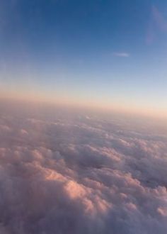 the view from an airplane window looking down on some clouds and blue sky in the distance