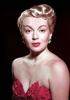 a woman in a red dress with flowers on her chest and hair pulled back to the side