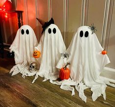 three halloween ghost statues sitting on the floor in front of a door with pumpkins and jack - o'- lanterns