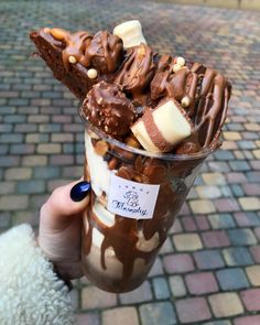 a person holding up a cup filled with chocolate and marshmallows on top of ice cream