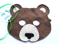 a brown bear mask with white eyes and green ribbon around the mouth on a white surface