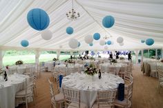 tables and chairs are set up in a large tent with white tablecloths and blue lanterns hanging from the ceiling