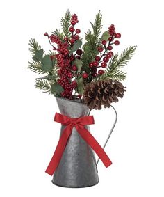 a metal vase with berries, pine cones and evergreen branches in it is tied with a red ribbon