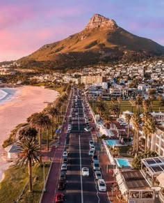 an aerial view of a beach town with mountains in the background and cars parked on the road