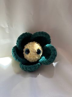 a small stuffed animal with big eyes in a crocheted green flower case on a white surface