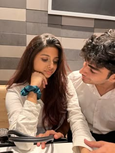 a man and woman sitting at a table looking at something