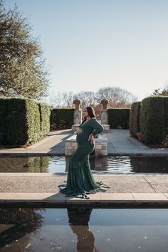 a woman standing in front of a fountain wearing a long green dress and posing for the camera