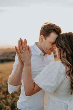 a man and woman standing in a field holding their hands together