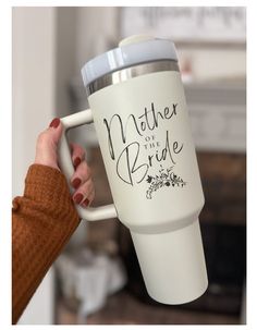 a woman holding a white coffee cup with the words mother of the bride on it