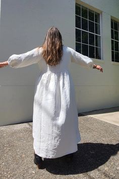 a woman in a white dress is walking towards a building with her arms spread out