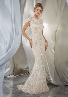 a woman in a white dress standing next to a silver backdrop and posing for the camera