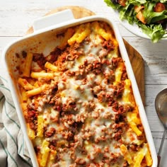 a casserole dish with meat and cheese on the side next to a salad