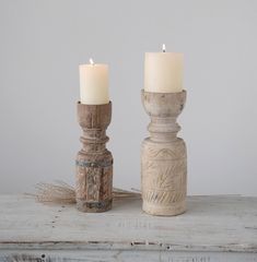 two candles are sitting next to each other on a white wooden table with a gray wall in the background