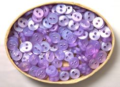 a wooden bowl filled with lots of purple buttons