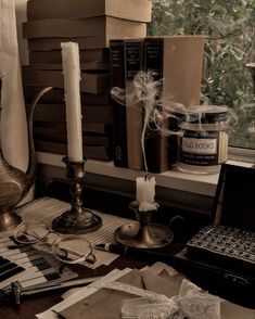 an assortment of books, candles and other items sit on a desk in front of a window