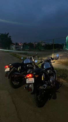 two motorcycles parked next to each other on the side of the road at night time