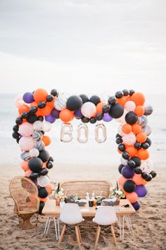 a table set up with balloons and chairs on the beach for an 60th birthday party