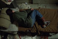 a man laying on top of a bed covered in pillows and blankets next to a pile of newspapers