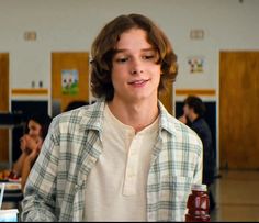 a young man holding a jar of peanut butter and looking at the camera with people in the background