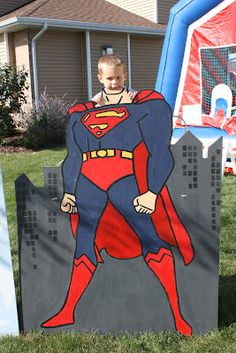 a young boy standing in front of a sign with a superman figure painted on it