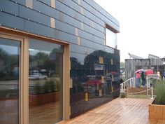 people are standing outside on the deck in front of a building with large windows and wooden floors