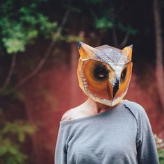 a man with an owl mask on his head standing in front of trees and bushes