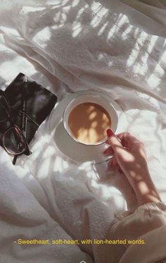 a person holding a cup of coffee on top of a bed