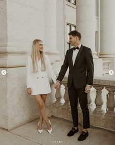 a man and woman holding hands while standing next to each other in front of a building